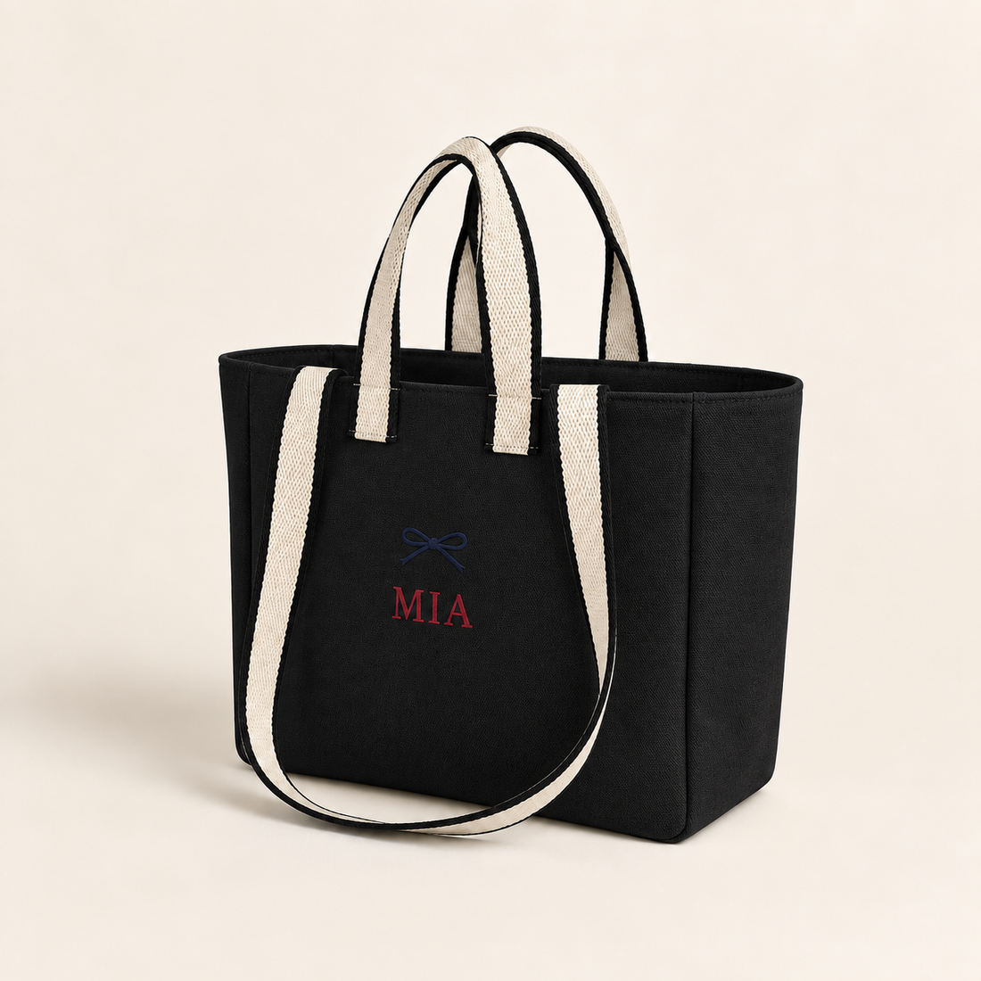 Black contrast-strap canvas tote with example navy bow and red MIA embroidery, angled view