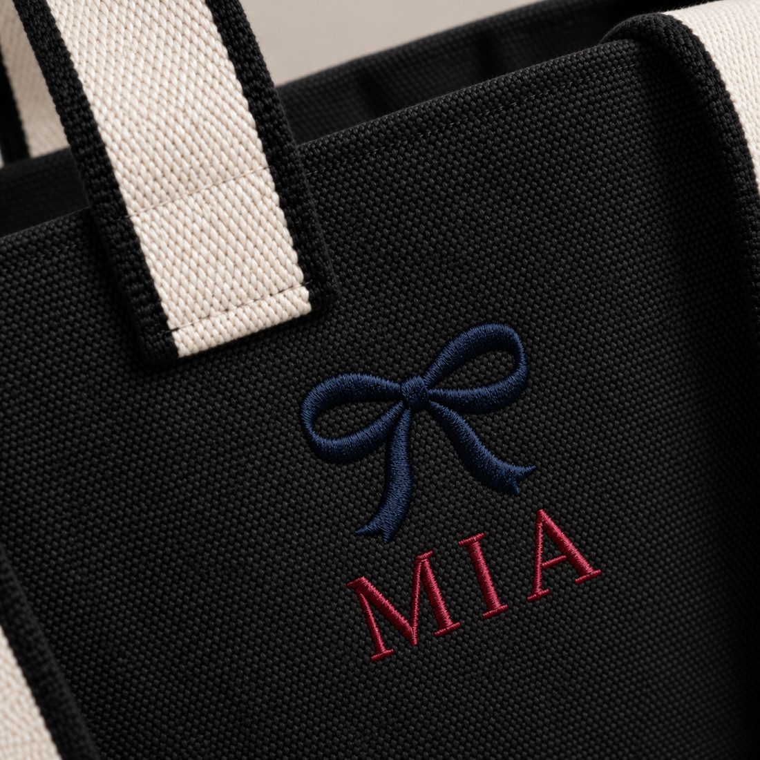 Close-up of example navy bow and red MIA embroidery on the Black contrast-strap canvas tote