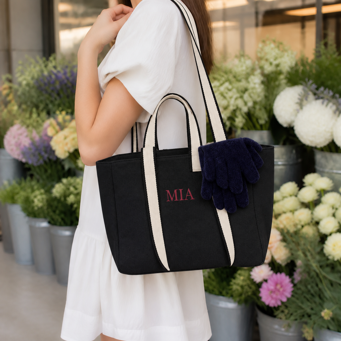 Woman carrying the Black contrast-strap canvas tote with example MIA embroidery past buckets of flowers