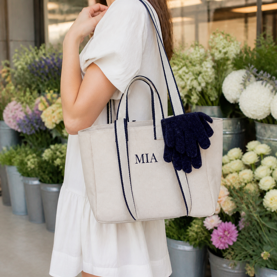 Woman carrying the Off White contrast-strap canvas tote with example bow and MIA embroidery past buckets of flowers